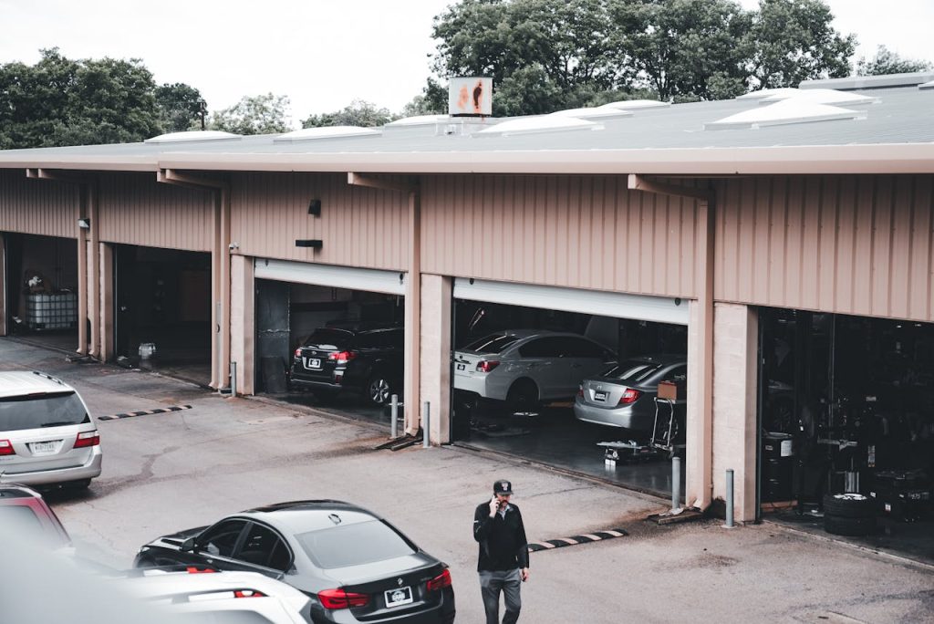 A man walks by a garage with cars parked inside and outside in an urban setting.